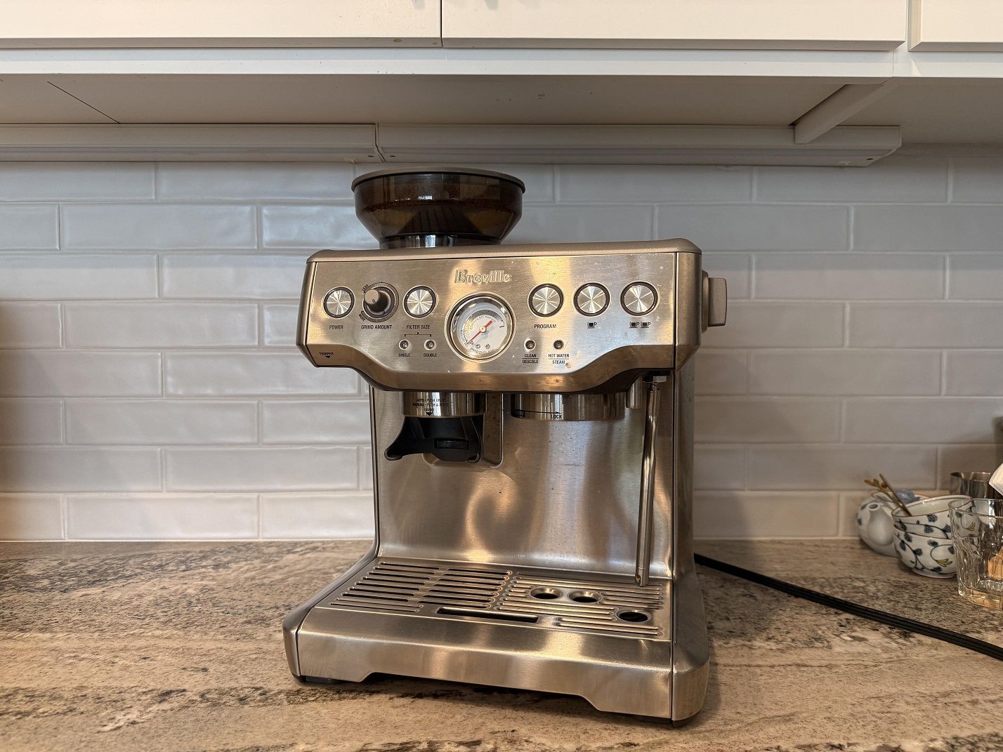 The Breville Barista Express home espresso machine against a tiled kitchen backsplash.