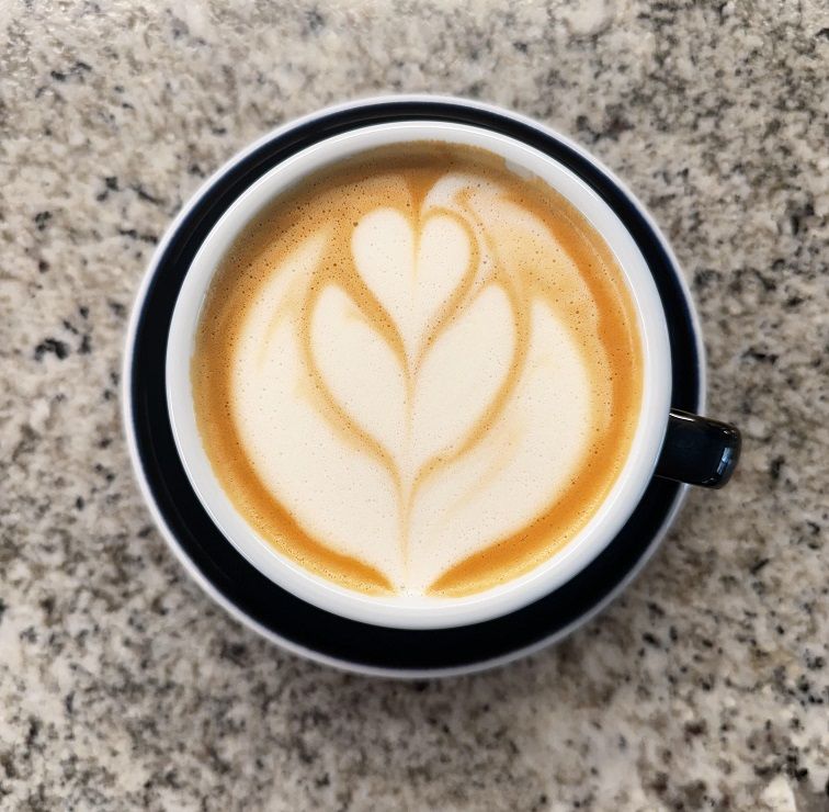 Close-up top-down view of a latte in a blue mug with a blue saucer. The latte has steamed milk art resembling an abstract tulip.