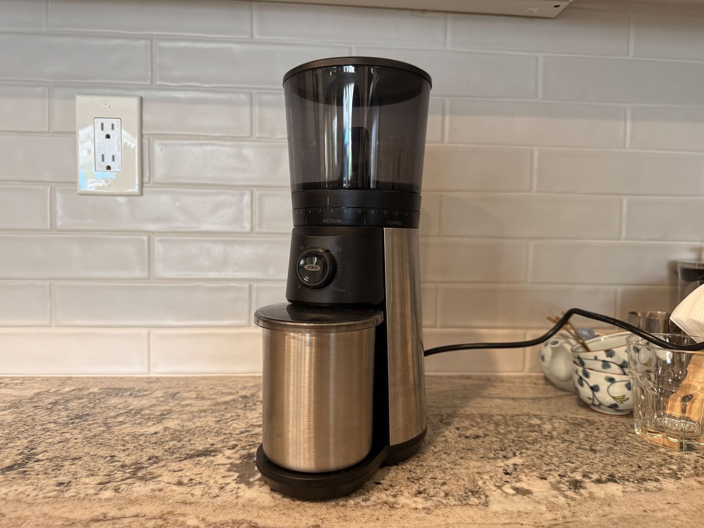 The OXO Brew Conical Burr Coffee Grinder against a tiled kitchen backsplash.