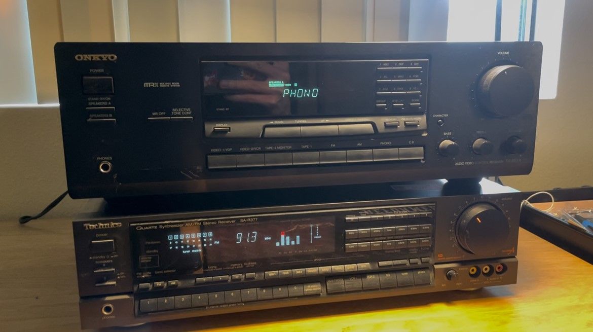 Two black stereo receivers stacked upon one another, both with bright blue indicator lights.